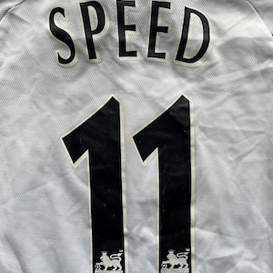 Puede incluir: Camiseta de f&uacute;tbol blanca con el nombre "SPEED" en letras negras grandes. Debajo, dos grandes n&uacute;meros negros "11". El logotipo de la Premier League est&aacute; en la parte inferior de cada n&uacute;mero.