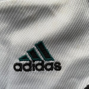 May include: White athletic jersey with a green and black Adidas logo.