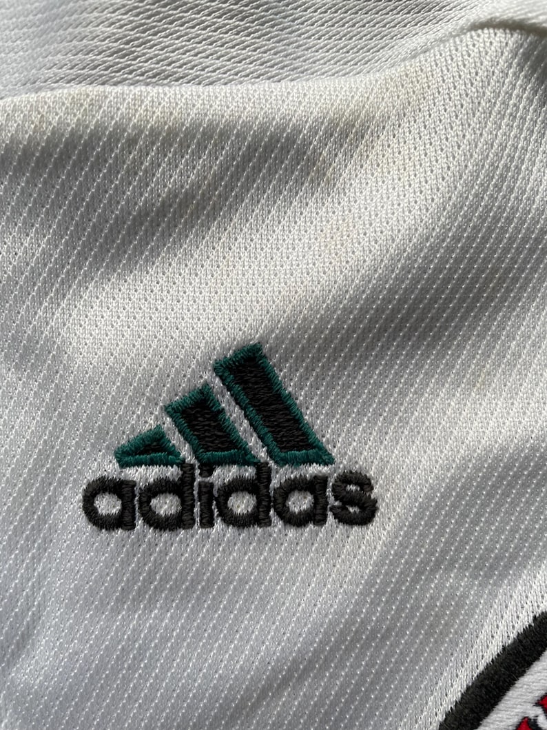 May include: White athletic jersey with a green and black Adidas logo.