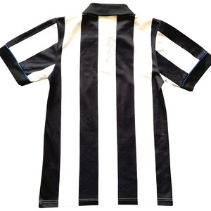 May include: A short-sleeved collared shirt with vertical black and white stripes. The shirt has a black collar and sleeve trim with a thin blue accent. The garment is made of a smooth, possibly synthetic fabric.