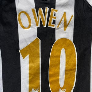 May include: Black and white striped soccer jersey with the name "OWEN" and the number "10" in gold on the back. The jersey has the Premier League logo on the bottom.