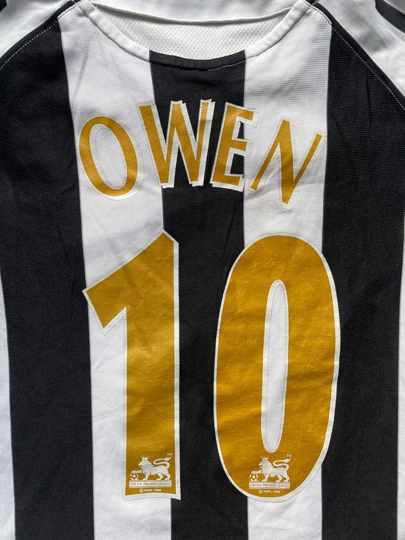 May include: Black and white striped soccer jersey with the name "OWEN" and the number "10" in gold on the back. The jersey has the Premier League logo on the bottom.