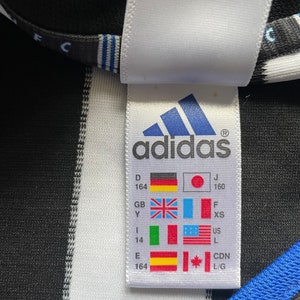 May include: White tag with black text and a black and white adidas logo. The tag shows size conversions for different countries, including Germany, Japan, United Kingdom, Italy, United States, Canada, and Spain.