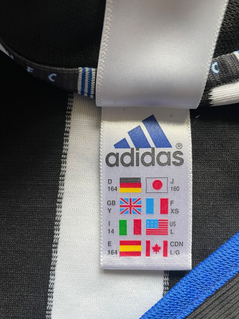 May include: White tag with black text and a black and white adidas logo. The tag shows size conversions for different countries, including Germany, Japan, United Kingdom, Italy, United States, Canada, and Spain.