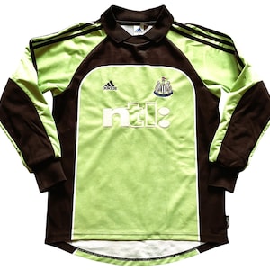 Pu&ograve; includere: Maglia da calcio a maniche lunghe verde lime e marrone, con il logo Adidas e lo stemma del Newcastle United. La maglia presenta la scritta "ntl:" in lettere bianche sul davanti.