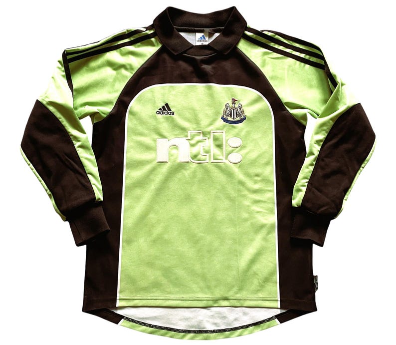 Pu&ograve; includere: Maglia da calcio a maniche lunghe verde lime e marrone, con il logo Adidas e lo stemma del Newcastle United. La maglia presenta la scritta "ntl:" in lettere bianche sul davanti.