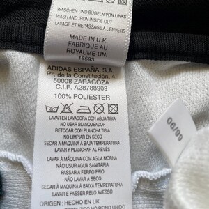May include: A close-up shot of a white clothing label with black text. The label details care instructions, including washing and ironing guidance. It also states "Made in U.K." and features the Adidas logo and address.