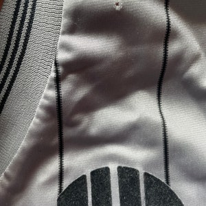May include: A gray and black striped jersey with a black logo on the front. The logo is a stylized letter "U" with a circle around it.