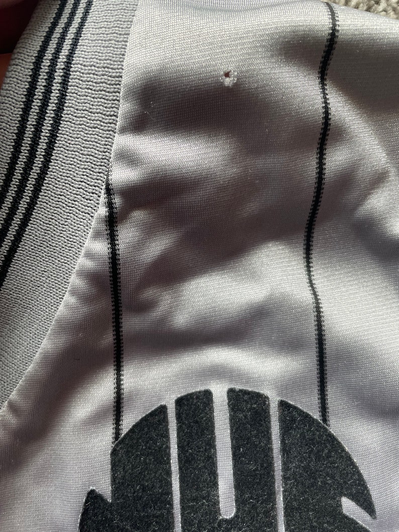 May include: A gray and black striped jersey with a black logo on the front. The logo is a stylized letter "U" with a circle around it.
