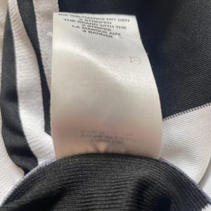 May include: White and black striped fabric with a white tag that reads "Die Weltmarke mit den 3 Streifen, The Brand with the 3 Stripes, La Marque aux 3 Bandes". The tag also includes the text "Made in Indonesia, Afrique du Podbr, ASR0005".