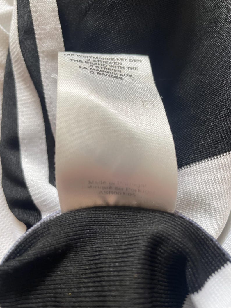 May include: White and black striped fabric with a white tag that reads "Die Weltmarke mit den 3 Streifen, The Brand with the 3 Stripes, La Marque aux 3 Bandes". The tag also includes the text "Made in Indonesia, Afrique du Podbr, ASR0005".
