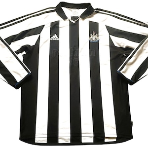 Puede incluir: Camiseta de f&uacute;tbol de manga larga a rayas blancas y negras con cuello. El logotipo de Adidas y el escudo del equipo son visibles en el pecho. Las mangas tienen rayas blancas y ribetes azules.