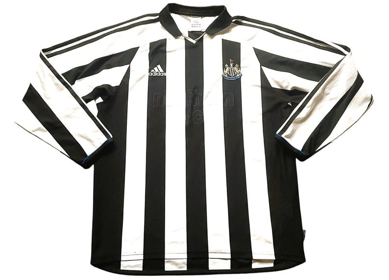 Puede incluir: Camiseta de f&uacute;tbol de manga larga a rayas blancas y negras con cuello. El logotipo de Adidas y el escudo del equipo son visibles en el pecho. Las mangas tienen rayas blancas y ribetes azules.