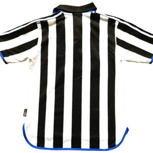 May include: Black and white striped football shirt with blue trim. The shirt has a collar and short sleeves.