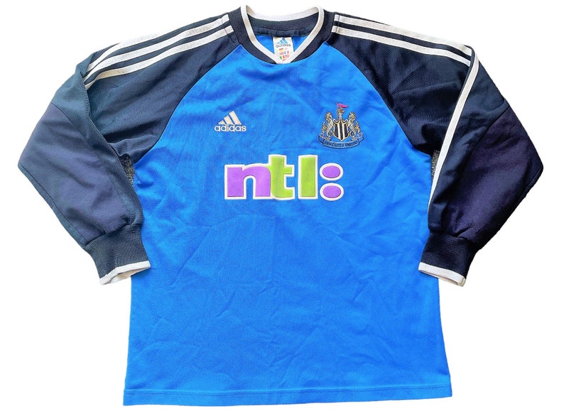 May include: A blue long-sleeved soccer jersey with black and white stripes on the shoulders. The jersey has the Adidas logo, the Newcastle United crest, and the NTL logo.