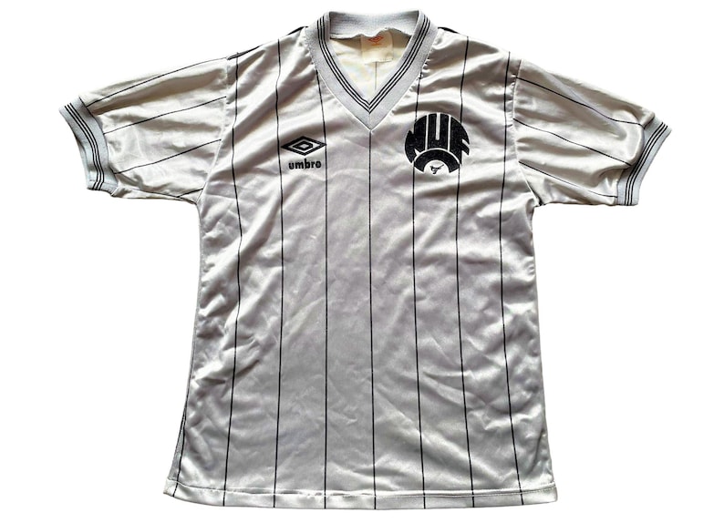 May include: A white and black striped soccer jersey with a black and white logo on the front. The logo says "MUF" and has a bull's head inside. The jersey has a v-neck and is made by Umbro.