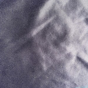 May include: Close-up of a dark navy blue fabric with a subtle textured pattern. The fabric has a slight sheen and appears to be tightly woven. The image shows the details of the material's surface, highlighting its texture and color variations.