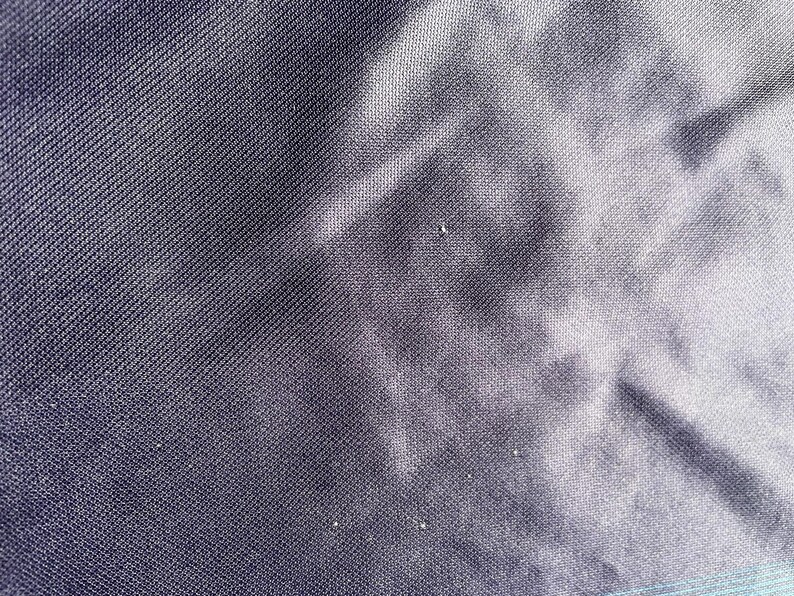 May include: Close-up of a dark navy blue fabric with a subtle textured pattern. The fabric has a slight sheen and appears to be tightly woven. The image shows the details of the material's surface, highlighting its texture and color variations.