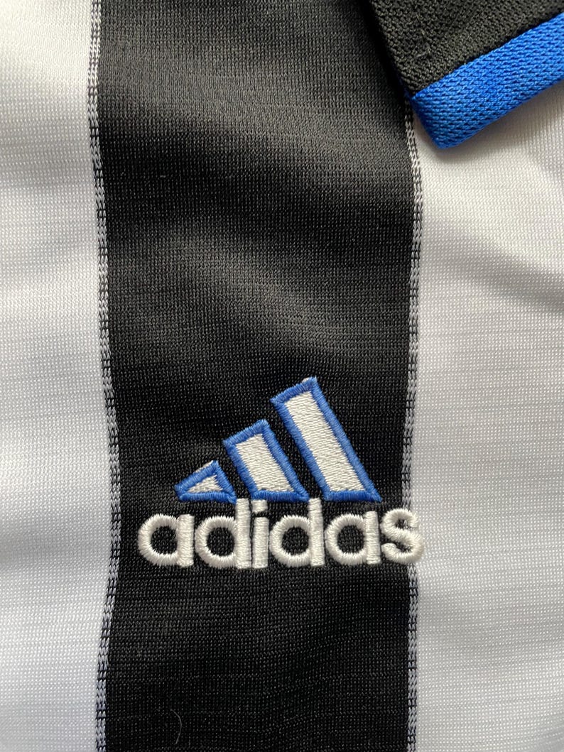 May include: A white and black striped soccer jersey with a blue and white Adidas logo embroidered on the front.