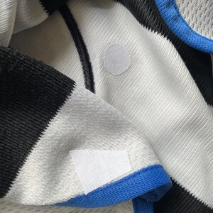 Puede incluir: Primer plano de una tela a rayas blancas y negras con ribete azul. Dos parches de tela blanca est&aacute;n cosidos en la tela.