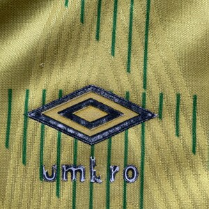 May include: A yellow and green soccer jersey with a diamond-shaped logo and the word "umbro" printed on the front.