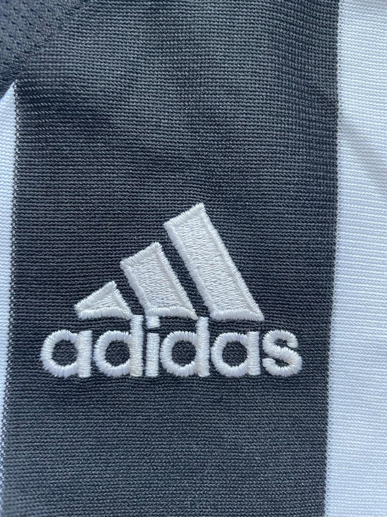May include: White adidas logo embroidered on a black fabric background.