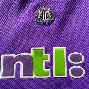 May include: A purple soccer jersey with a white and black crest and the word "ntl" in green and purple letters.