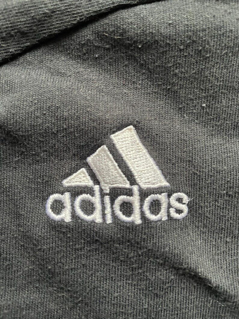 May include: A black Adidas logo with white stitching on a black fabric background.