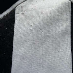 May include: Close-up of a white and black striped fabric. The fabric has a textured surface with a white border and a blue accent. The image focuses on the details of the material.