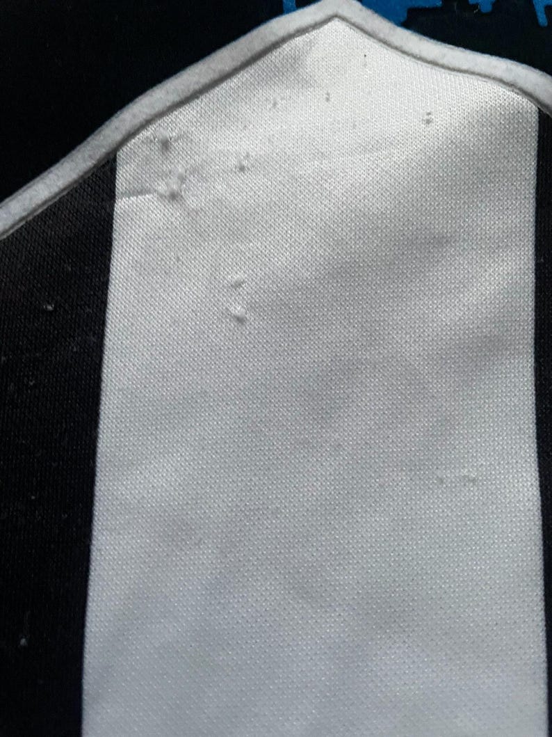 May include: Close-up of a white and black striped fabric. The fabric has a textured surface with a white border and a blue accent. The image focuses on the details of the material.