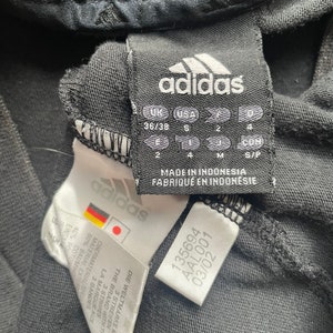 May include: Black adidas shirt tag with size information in UK, USA, and European sizes. The tag also includes the text "Made in Indonesia" and "Fabriqu&eacute; en Indon&eacute;sie".