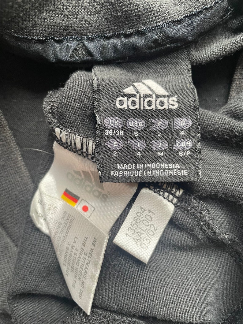 May include: Black adidas shirt tag with size information in UK, USA, and European sizes. The tag also includes the text "Made in Indonesia" and "Fabriqu&eacute; en Indon&eacute;sie".