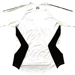Pode incluir: Camisa esportiva branca com detalhes em preto nas laterais e mangas. A camisa tem gola redonda e o logotipo da Adidas na parte superior das costas. As mangas t&ecirc;m tr&ecirc;s listras pretas.