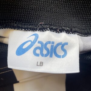 May include: Close-up of a white tag with the blue "asics" logo and the letters "LB". The tag is sewn onto black and white fabric.