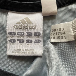 Pu&ograve; includere: Etichetta bianca con logo adidas nero e testo. L'etichetta contiene informazioni sulle taglie in taglie UK, USA, F, D, E, I, J e CON. L'etichetta contiene anche il testo "Made in Tunisia, Fabrique en Tunisie" e la data 08/03, 021784, AHJ001.