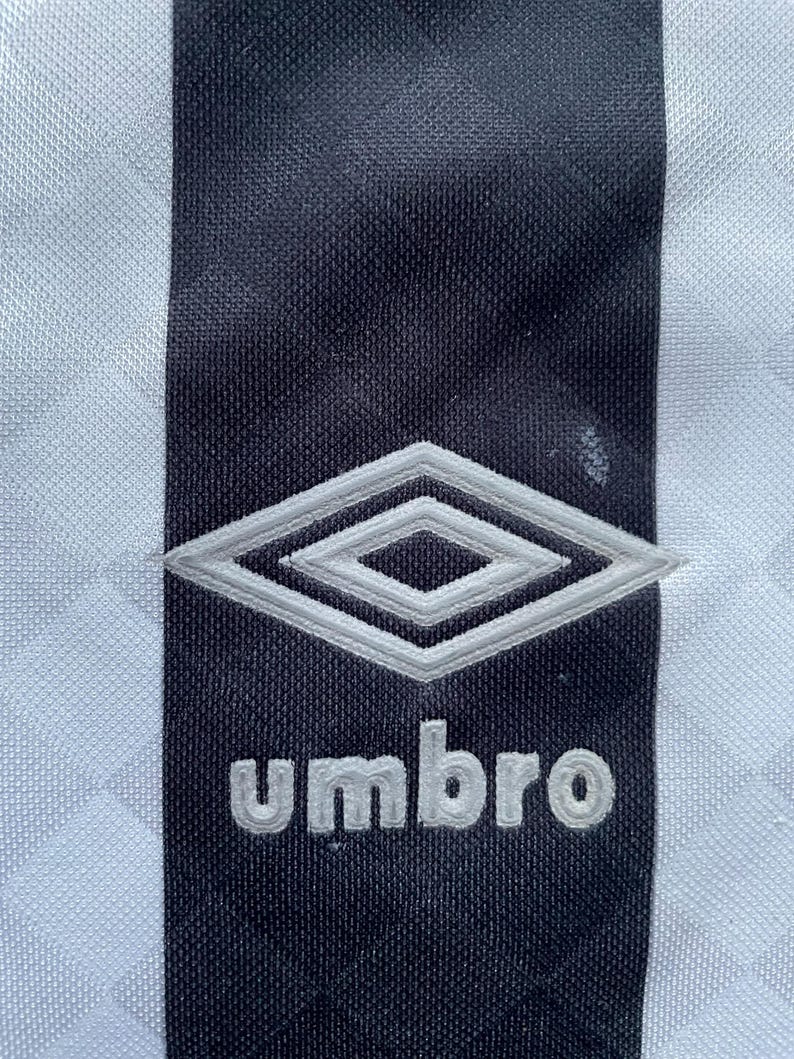 May include: A black and white striped soccer jersey with a white diamond logo and the word "umbro" in white lettering.