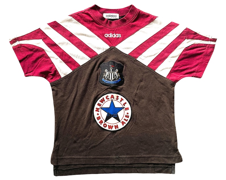 Puede incluir: Una camiseta de f&uacute;tbol Adidas Newcastle United vintage. La camiseta presenta un dise&ntilde;o a rayas granate y blancas en los hombros y las mangas, con un panel frontal marr&oacute;n. El logotipo de Newcastle Brown Ale y el escudo del equipo son visibles.