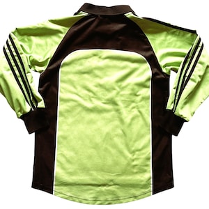 Pu&ograve; includere: Una maglia sportiva a maniche lunghe verde lime e marrone. La maglia presenta un colletto e maniche marroni, con pannelli verde lime sul davanti e sul retro. Strisce nere adornano le maniche. La maglia &egrave; realizzata in materiale liscio.