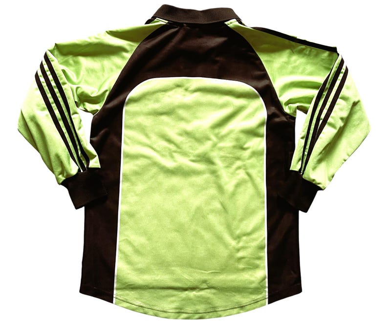 Pu&ograve; includere: Una maglia sportiva a maniche lunghe verde lime e marrone. La maglia presenta un colletto e maniche marroni, con pannelli verde lime sul davanti e sul retro. Strisce nere adornano le maniche. La maglia &egrave; realizzata in materiale liscio.