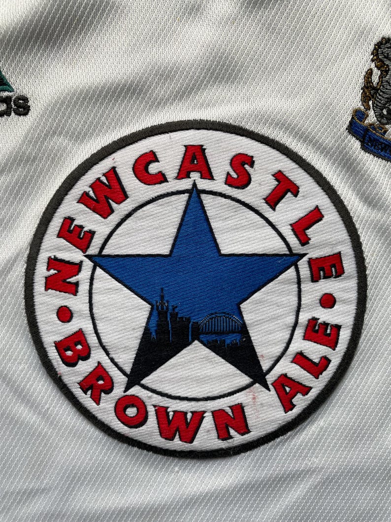 May include: A white patch with a black circle and a red and blue star. The circle has the text "NEWCASTLE BROWN ALE" around the edge.