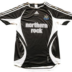 Pu&ograve; includere: Maglia da calcio bianca e nera con la scritta "northern rock". La maglia presenta inserti e maniche bianche, con il logo Adidas e lo stemma della squadra. Taglia M.