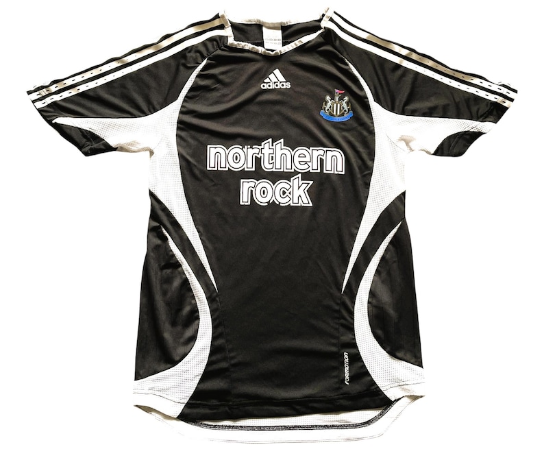 Pu&ograve; includere: Maglia da calcio bianca e nera con la scritta "northern rock". La maglia presenta inserti e maniche bianche, con il logo Adidas e lo stemma della squadra. Taglia M.