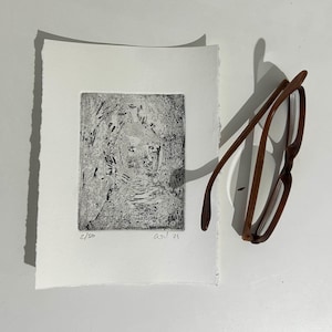 May include: Black and white print of a portrait with the text "2/50" and "axt 21" in the bottom corners.