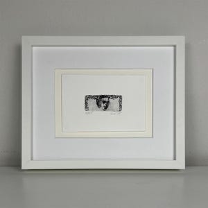May include: A framed black and white etching of a face surrounded by a wreath. The etching is titled "Goats" and is signed "6/25".