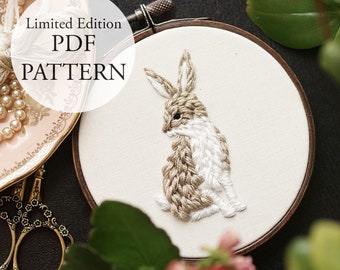May include: A limited edition PDF pattern for embroidery featuring a brown and white rabbit sitting on a white fabric background. The rabbit is surrounded by a wooden embroidery hoop.