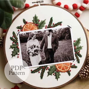 May include: Embroidered hoop art featuring a black and white photo of a couple, surrounded by green holly leaves, red berries, and orange slices. The text "PDF Pattern" is visible in the lower left corner.
