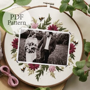May include: A white embroidery hoop with a black and white photo of a couple in the center. The photo is surrounded by embroidered flowers, leaves, and bees in shades of pink, green, and yellow.
