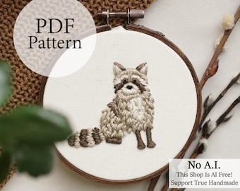 May include: An embroidery hoop featuring a detailed raccoon design. The raccoon is stitched with shades of brown and gray, with a striped tail. The text "PDF Pattern" is in a white circle. The text "No A.I. This Shop Is AI Free! Support True Handmade" is in a white rectangle.