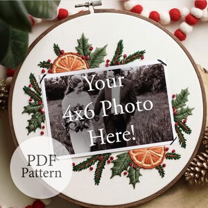 May include: A white embroidery hoop with a Christmas-themed design featuring holly leaves, red berries, and orange slices. The hoop includes a space for a 4x6 photo with the text "Your 4x6 Photo Here!" and the words "PDF Pattern" at the bottom.