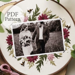 May include: A white embroidery hoop with a black and white photo of a couple in the center. The photo is surrounded by embroidered flowers, leaves, and bees in shades of pink, green, and yellow.